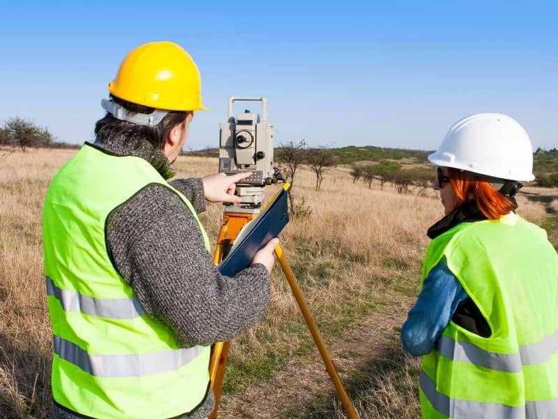 Land surveyor using surveying equipment to measure property boundaries on a development site