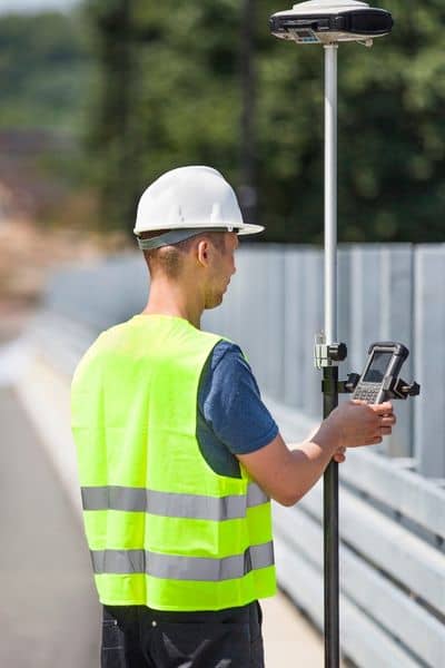 Land surveyor using GPS equipment to collect property boundary data during field work that affects land survey cost